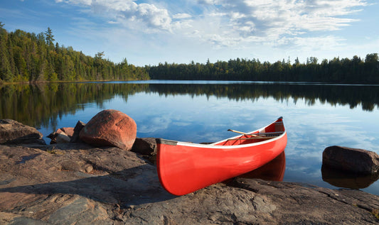 A red canoe sitting on the shores of a blue reflective lake in the Boundary Waters Canoe Area in Northern Minnesota