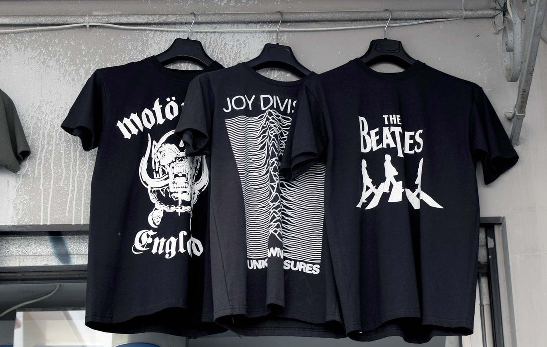 Three vintage black graphic tees with band logos hanging in a store