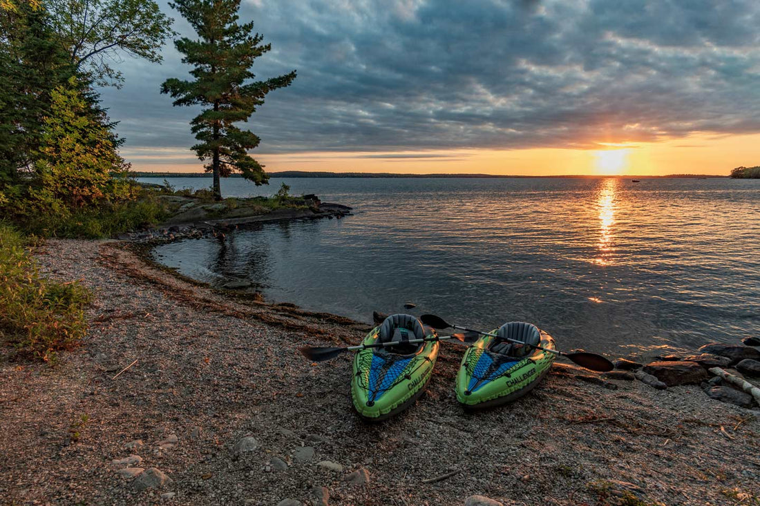 Two kayaks sitting on the beach of Lake Kabetogama in Voyageurs National Park as the sun sets over the water in the background